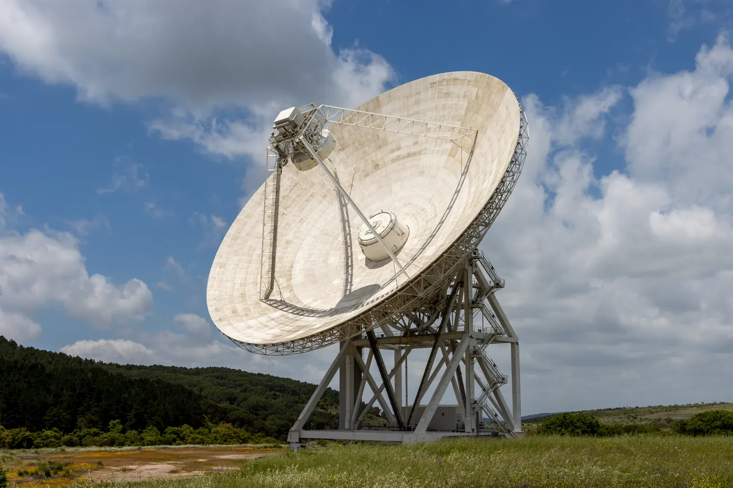 Grande radiotelescópio apontado para o céu, visto contra uma paisagem aberta